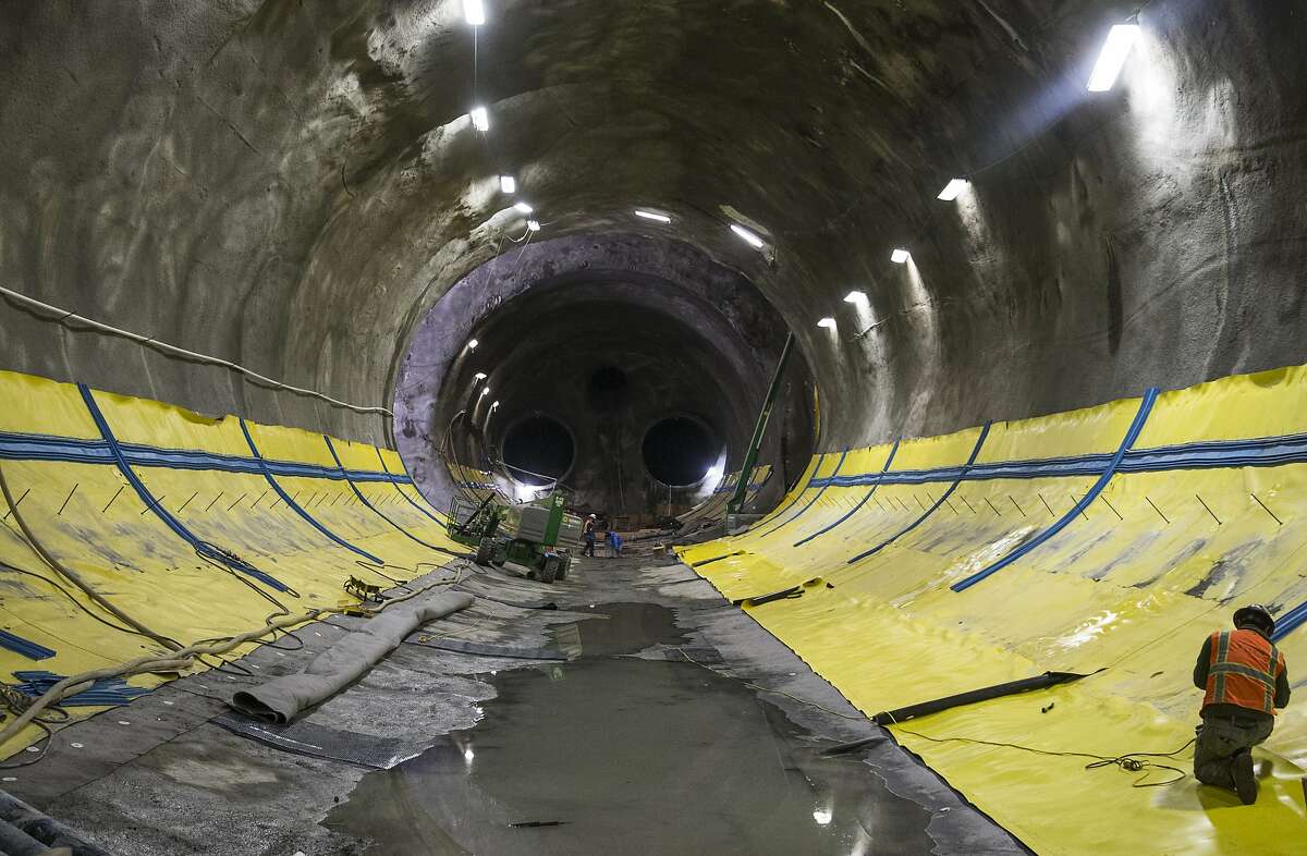 A man secures large yellow tarps as part of a waterproofing procedure during construction on the Central Subway near Stockton and Washington streets Tuesday, April 3, 2018 in San Francisco, Calif.