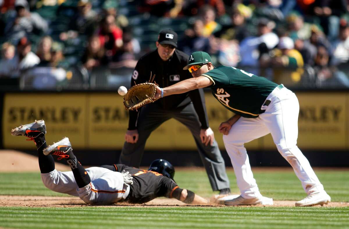 San Francisco Giants' Gregor Blanco, left, slides safely back into first as Oakland Athletics first baseman Matt Olson takes the pickup throw during the sixth inning of a Major League Baseball game, Sunday, March 25, 2018 in Oakland, Calif.