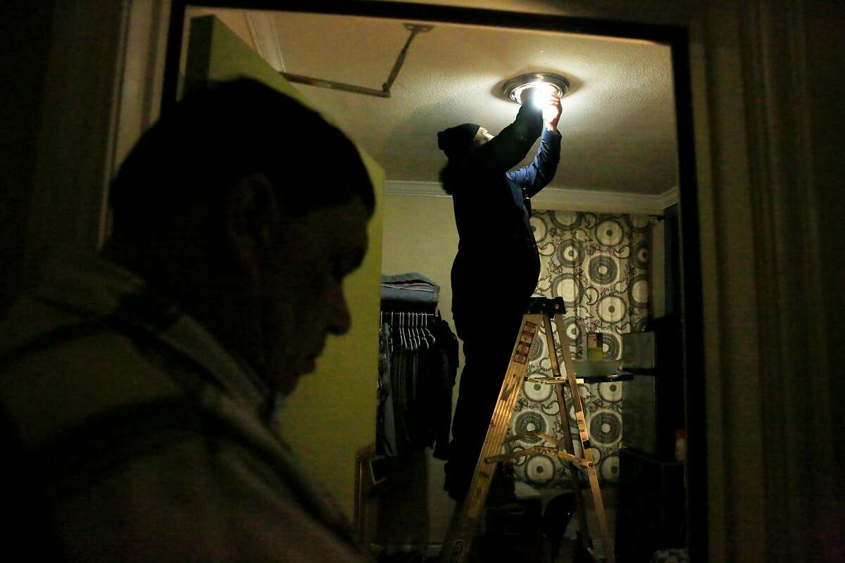 Tito Solifona (right), maintenance technician, replaces old bulbs with new LED bulbs in James Monson's (not shown) unit at a community housing development run by Swords to Plowshares on Tuesday, April 10, 2018, in San Francisco, Calif. San Francisco's Department of the Environment is providing 100,000 free LED lightbulbs to city residents, particularly disadvantaged ones under a new program.