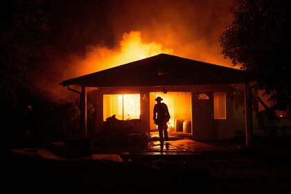 A firefighter approaches a burning residence as the Clayton Fire burns through Lower Lake, Calif.
