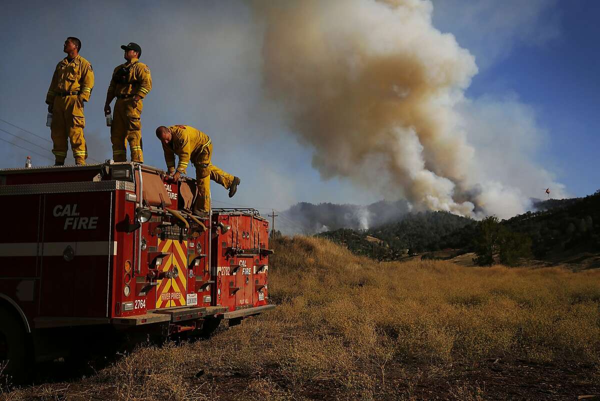 Cal Fire firefighters from Amador, Andrew Paik, left, Alex Salazar and Munir Massoud take a break after a full shift of fighting the fire as the Rocky Fire burns off of highway 20 behind them and in front of them August 3, 2015 in Lake County, Calif.