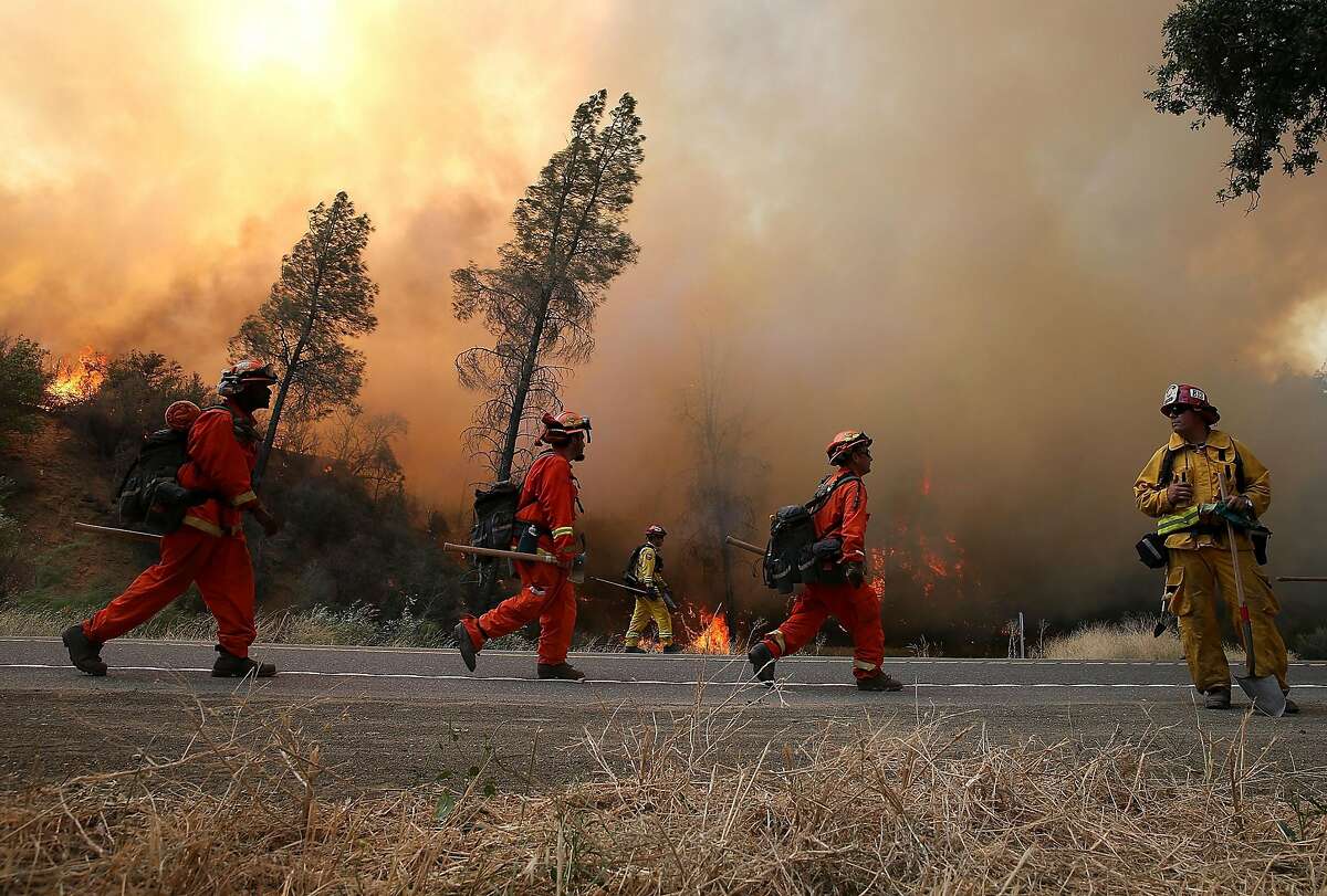 CLEARLAKE, CA - AUGUST 03: Inmate firefighters march along highway 20 as they conduct a backfire operation to head off the Rocky Fire on August 3, 2015 near Clearlake, California. Nearly 3,000 firefighters are battling the Rocky Fire that has burned over 60,000 acres has forced the evacuation of 12,000 residents in Lake County. The fire is currently 12 percent contained and has destroyed at least 14 homes. 6,300 homes are threatened by the fast moving blaze. (Photo by Justin Sullivan/Getty Images)