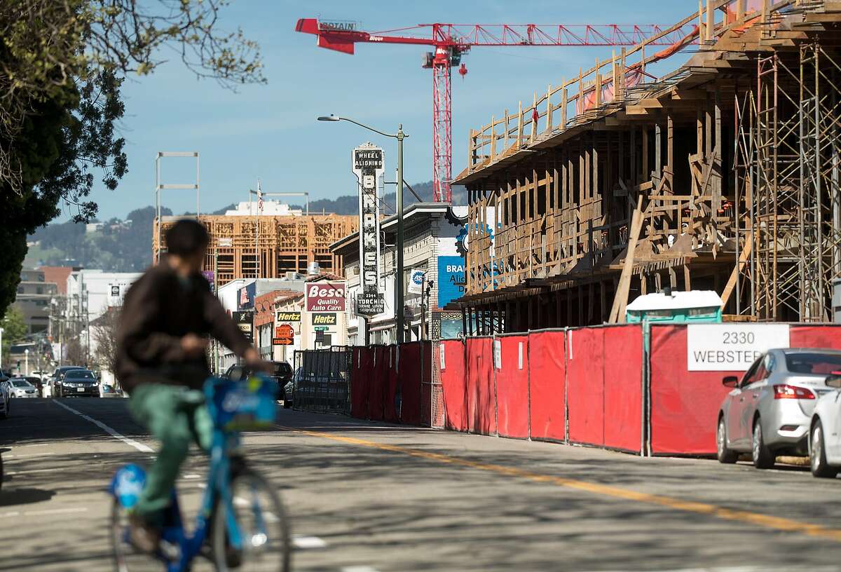 A bicyclist rides down Webster St., where new housing developments rise above decades-old automotive shops, on Friday, April 13, 2018, in Oakland, Calif.