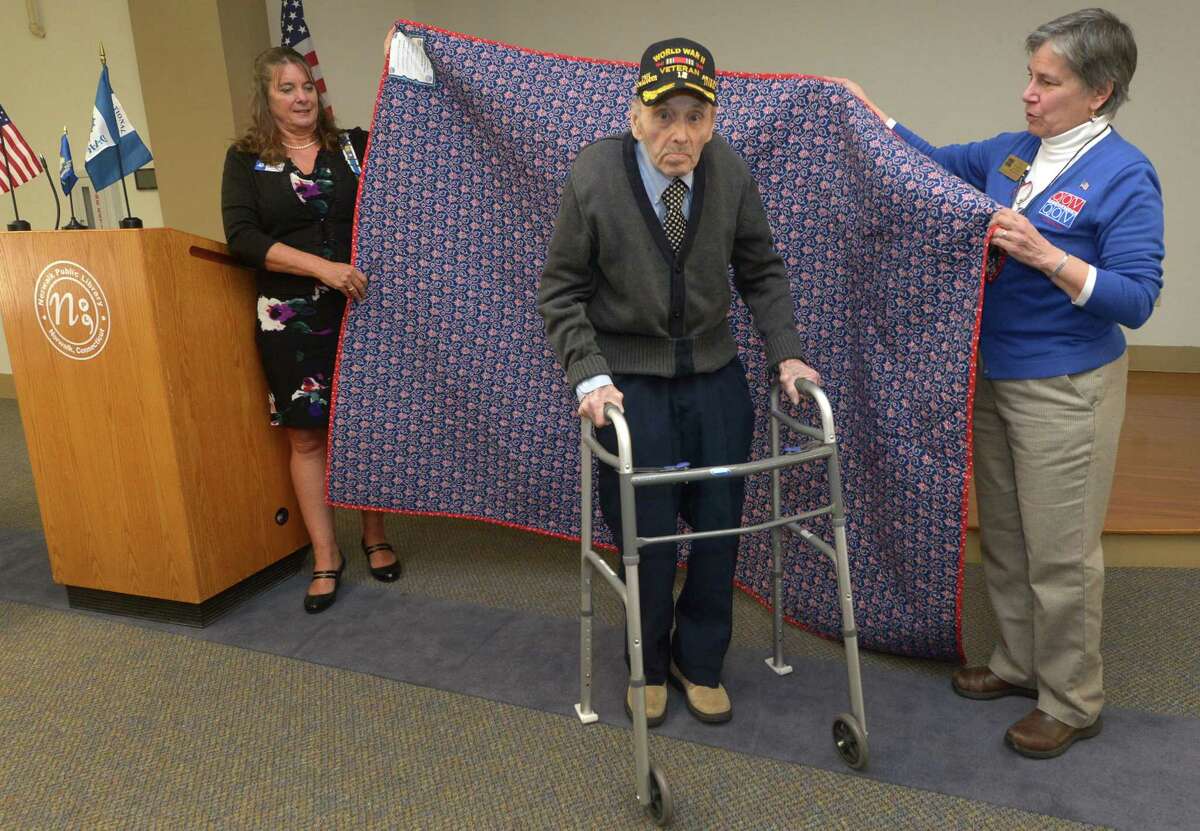 Quilt maker and DAR member Lisa Grant Wilson and Quilts of Valor CT State Coordinator Jane Dougherty wrap WWll Army veteran David Evans as notable Norwalk veterans are presented with patriotic quilts by Daughters of the American Revolution during a Quilts of Valor ceremony Saturday, April 14, 2018, at the South Norwalk Library in Norwalk, Conn.