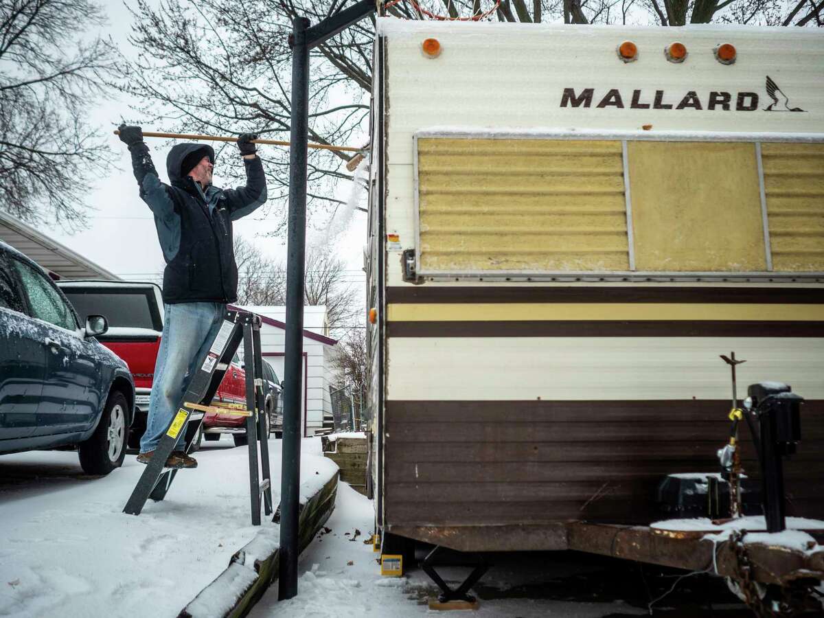 Aaron Manthei brushes snow and ice off of his camper during a storm Saturday, April 14, 2018, in Rochester, Minn. A storm system stretching from the Gulf Coast to the Great Lakes buffeted the central U.S. with heavy winds, rain, hail and snow, (Joe Ahlquist /The Rochester Post-Bulletin via AP)