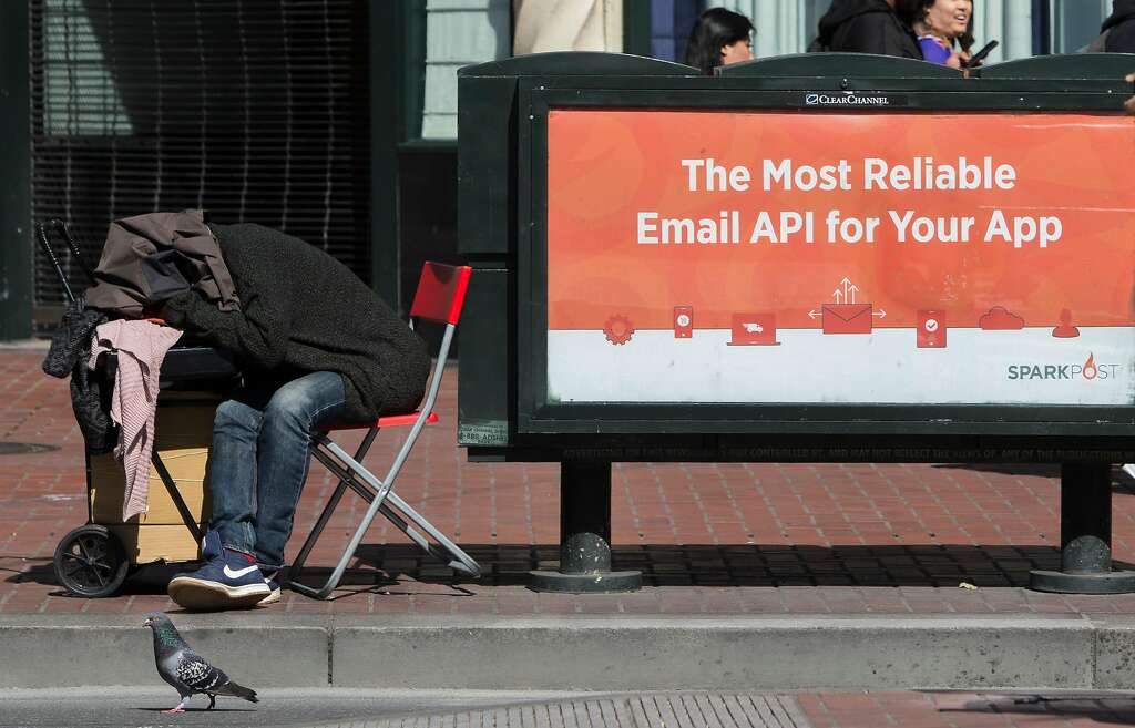 A man sleeps on a chair next to an advertisement for an app on Market Street. Photo: Jessica Christian / The Chronicle