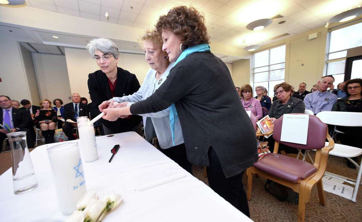 Holocaust survivor Hannah Kuperstoch, center, lights one of six candles during the observance with the help of her daughter, Mim Ramadei, right, and Barbara Katz.