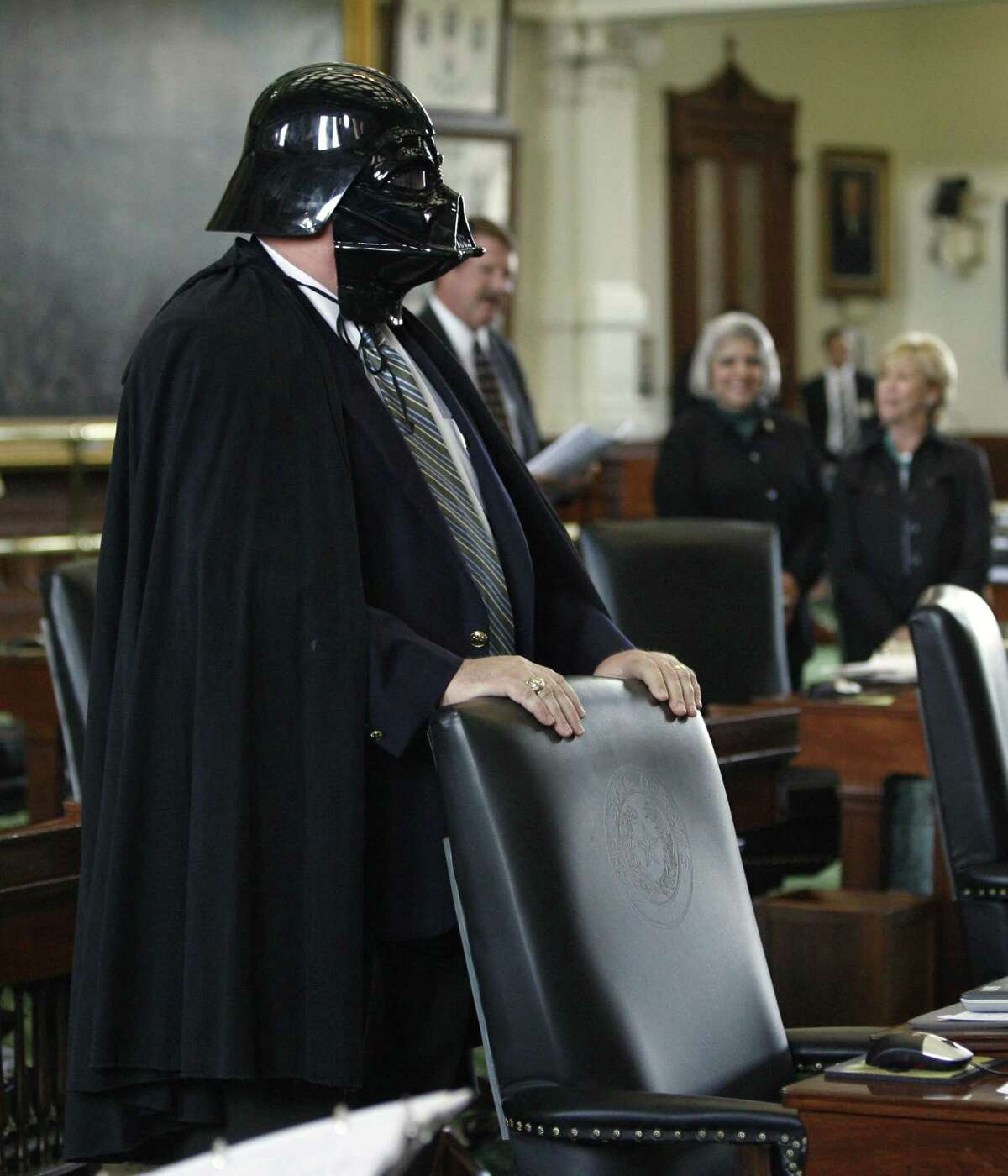 Sen. Tommy Williams, R-The Woodlands, stands at his desk wearing a Darth Vader mask and cape during the session in the Texas Senate, Thursday, May 10, 2007, in Austin, Texas. In the background are, from left, Sen. Mike Jackson, R-La Porte, Sen. Judith Zaffirini, D-Laredo, and Sen. Florence Shapiro, R-Plano. The costume was a response to a newspaper editorial calling Williams the "prince of darkness." (AP Photo/Harry Cabluck)