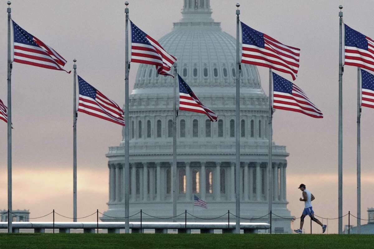 An early morning runner in 2017 crosses in front of the U.S. Capitol as he passes the flags circling the Washington Monument in Washington.