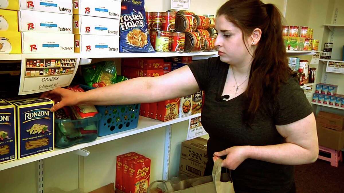 In this April 10, 2018 frame grab from video, student Hannah Daignault fills a grocery bag at the Schenectady County Community College food pantry in Schenectady, N.Y. As a 22-year-old student living on her own, Daignault finds it hard to stretch her student loans to cover the rising cost of books and fees, let alone food and rent, so she was thrilled when a campus food pantry opened last year. New York is the nation's first state to require free food pantries on all its public college campuses (AP Photo/Michael Hill)