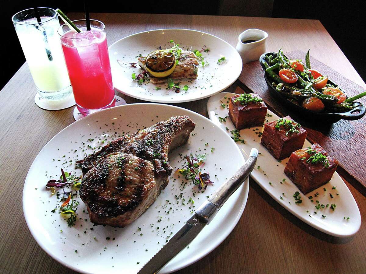 Clockwise from bottom left: double-cut pork chop, Bexar Chilcano cocktail, housemade ginger beer, six-ounce grilled red snapper fillet, blistered tomatoes and green beans side dish and a potato pavé side dish from Maverick Texas Brasserie