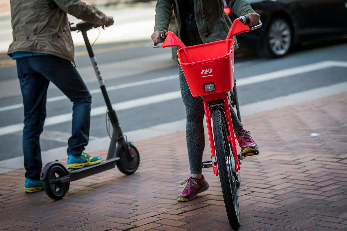 People ride a Uber Technologies Inc. Jump Bike pedal electric bicycle, right, and a Bird Rides Inc. shared electric scooter in San Francisco, California, U.S., on Friday, April 13, 2018. GPS-enabled�scooters�and bicycles are spreading across several major U.S. cities, driven by a wave of venture capital into a handful of companies.�Policymakers are scrambling to find ways to regulate the�great scooter boom of 2018. Photographer: David Paul Morris/Bloomberg