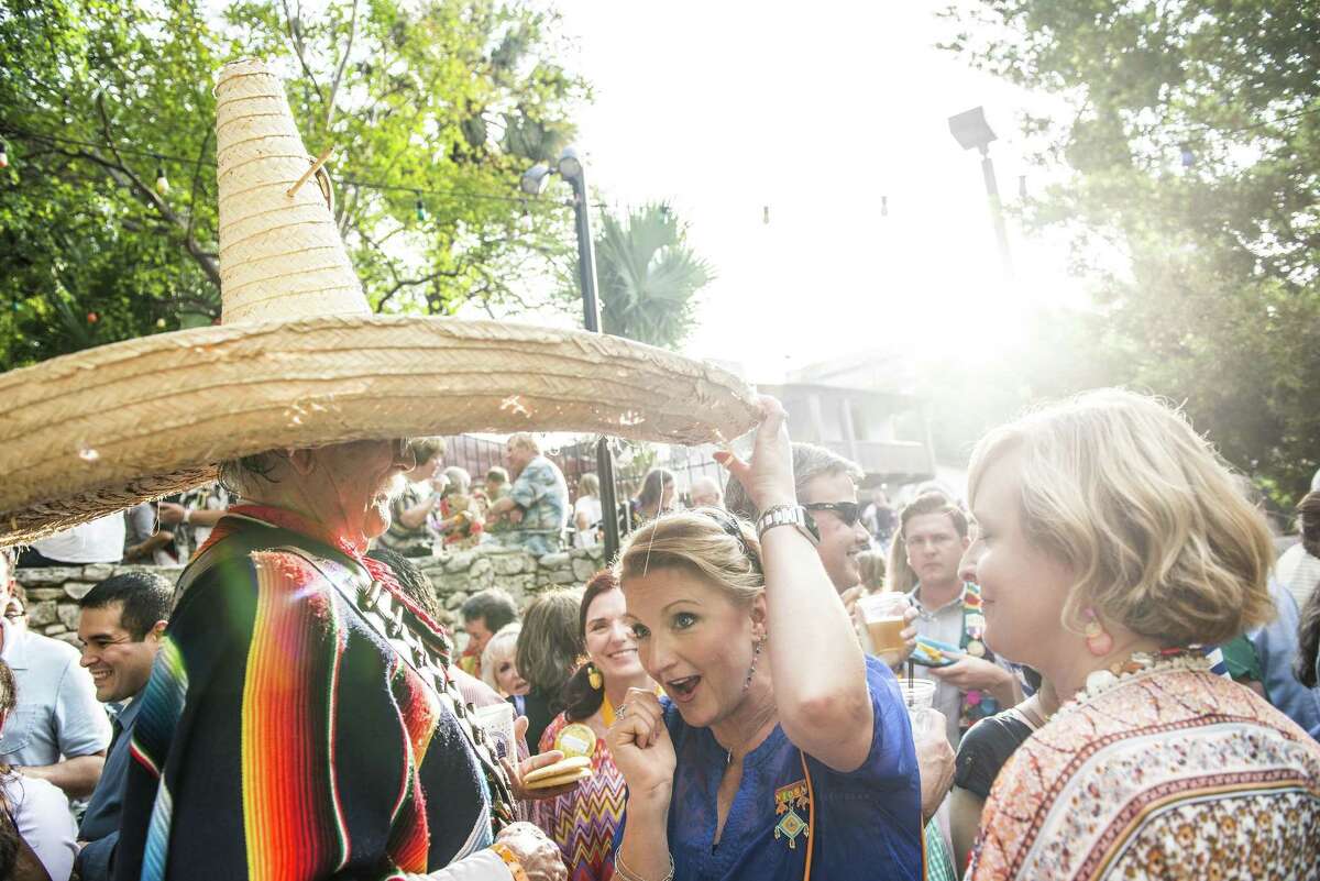 A woman tries to hide under Lloyd Jary or "Poncho Villita's" 30+ year old sombrero as he greets friends at NIOSA during Fiesta week in San Antonio, Texas in La Villita on Tuesday, April 19, 2016.