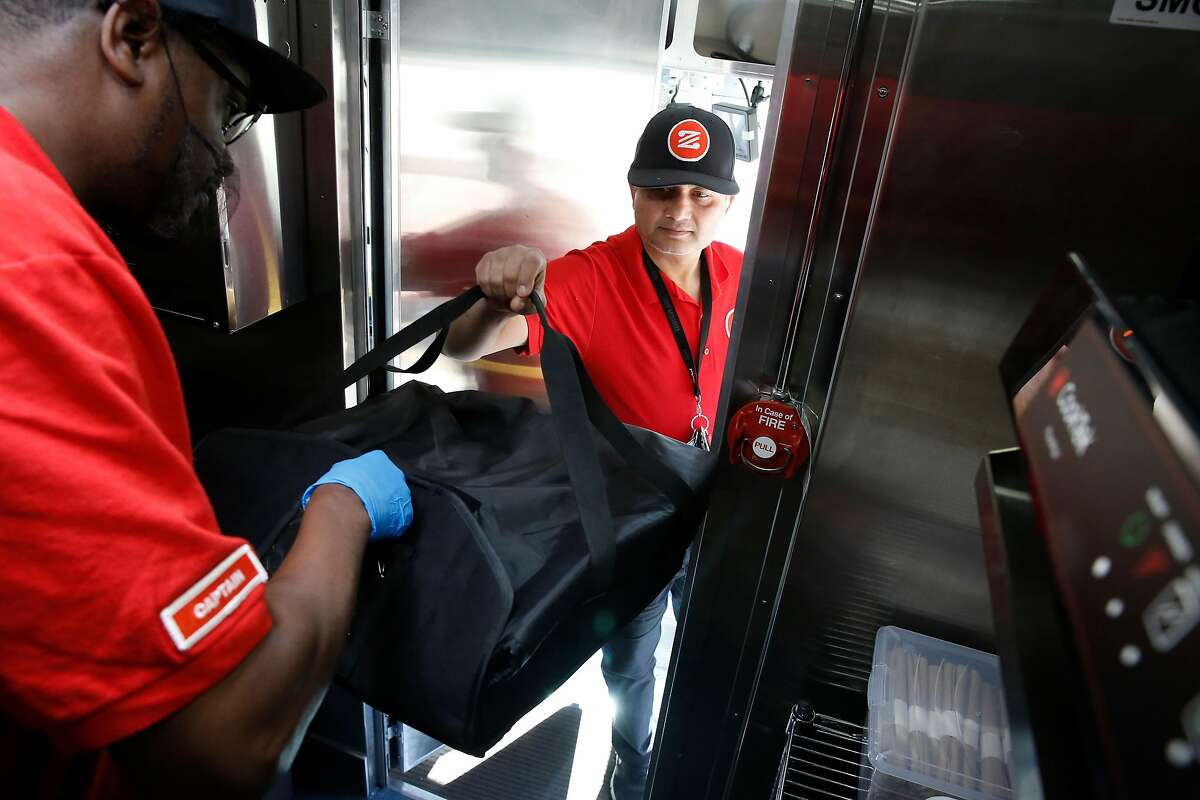Zume Captain Skylar Morris, ( left) the "Pielot" of this truck crew hands off a pizza for delivery to driver Deepak Dabadi in Palo Alto, Calif., Ca., on Tues. April 17, 2018. Zume Pizza uses robotic pizza-makers and smart ovens inside a truck to deliver cooked-to-order pizzas to customers.