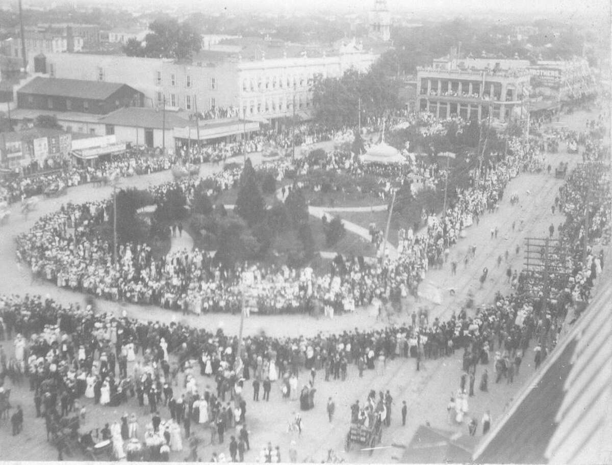 Looking southeast from Maverick Bank Building toward Alamo Plaza during the Battle of Flowers Parade c. 1898. Steeple of St. Joseph's Church under construction in distance.