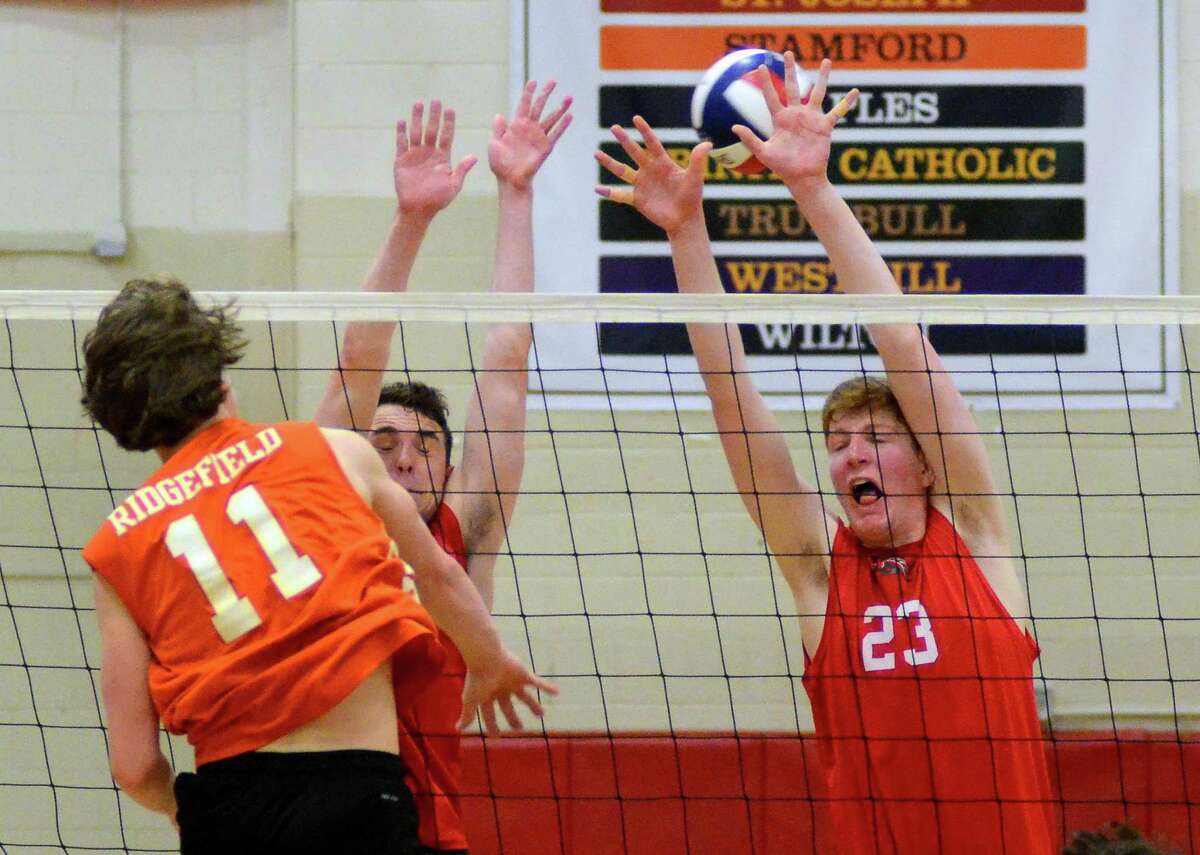 Ridgefield's Andrew Knachel (11) spikes the ball past Fairfield Warde's Luke Adelstein (23), at right, during boys volleyball action in Fairfield, Conn., on Wednesday Apr. 25, 2018. Attempting to block with Adelstein is teammate Luke Connor (3).