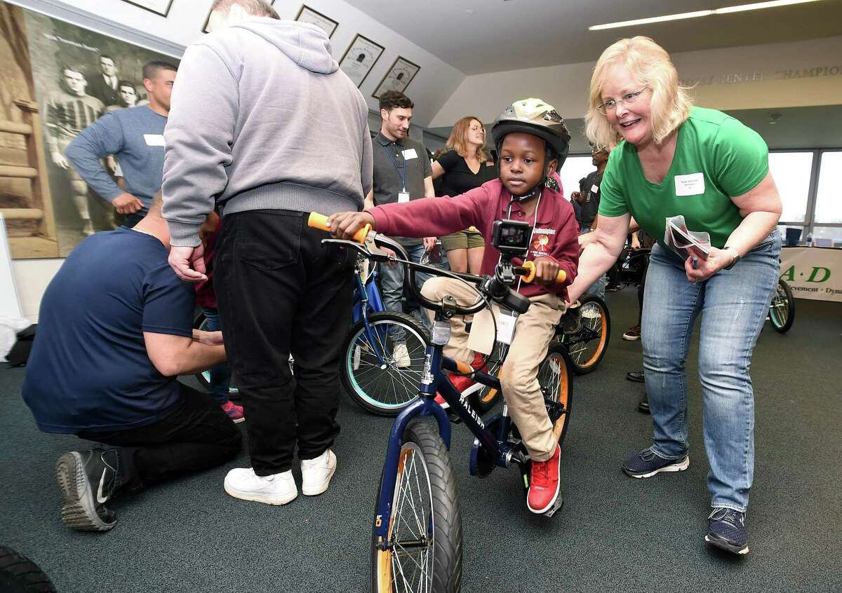 Jonah Ssemwizi (center) of Quinnipiac Stem School tries out a new bicycle with the help of Susan Wheeler in the Champions Room of Yale University's Kenney Center in New Haven on April 27, 2018. Wheeler was among teams of Yale University employees that assembled new bicycles as part of a team building project for students from Quinnipiac Stem School selected based on their kindness writing journal entries.