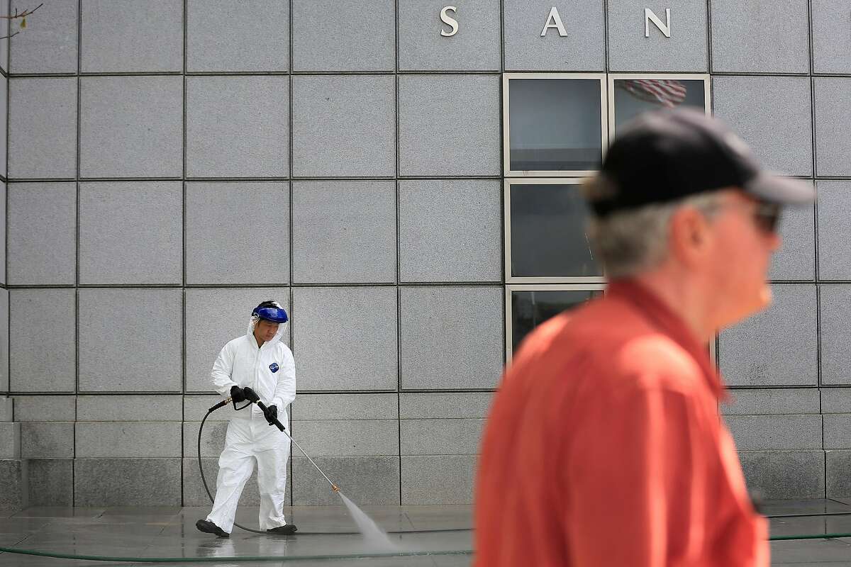 Austin Huang (left), custodian, uses a pressure washer as he cleans outside the main library as a pedestrian passes by on Friday, April 27, 2018 in San Francisco, Calif.