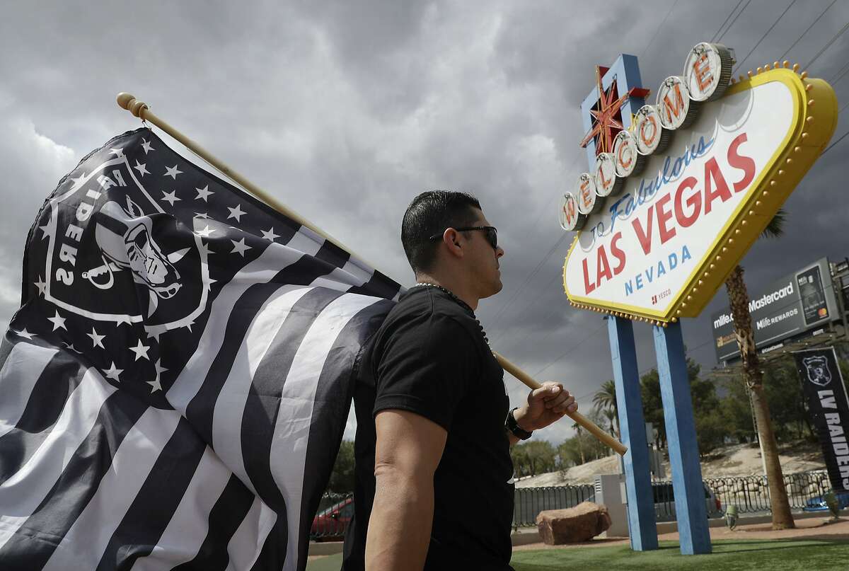 Matt Gutierrez carries a raiders flag by a sign welcoming visitors to Las Vegas, Monday, March 27, 2017, in Las Vegas. NFL team owners approved the move of the Raiders to Las Vegas in a vote at an NFL football annual meeting in Phoenix. (AP Photo/John Locher)
