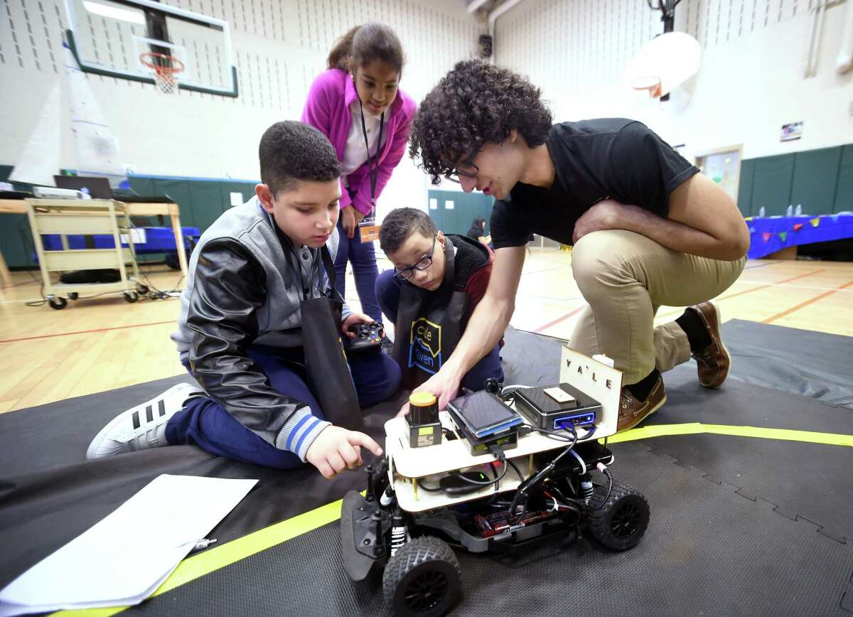 Left to right, Persio Anthony Veras, 11, Maria Gutierrez, 12, and Jeciel Jandel Suarez Valcarcel, 12, of Fair Haven School listen to Yale University students Omid Rooholfada talk about the unhackable self-driving car being developed by Y-Driving, a segment of the Flint Research Group, during a Code Haven Project Fair at Bishop Woods School in New Haven on April 27, 2018.