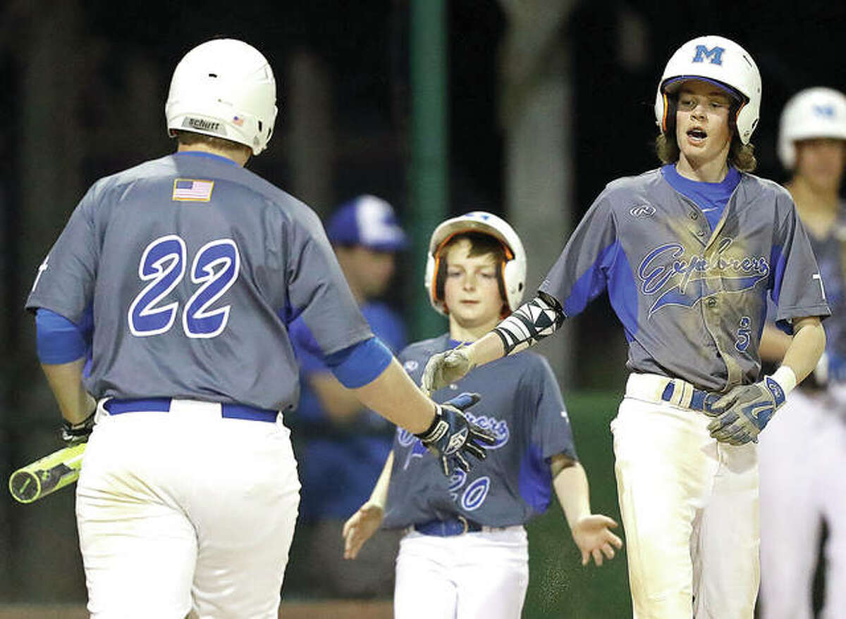 Marquette’s Brandon Lloyd (3) and Will Hurst (22) are congratulated by bat boy Will Fahnestock (20) after they scored in Monday night’s game against Belleville Althoff at Lloyd Hopkins Field in Gordon Moore Park. The Explorers won 6-0.
