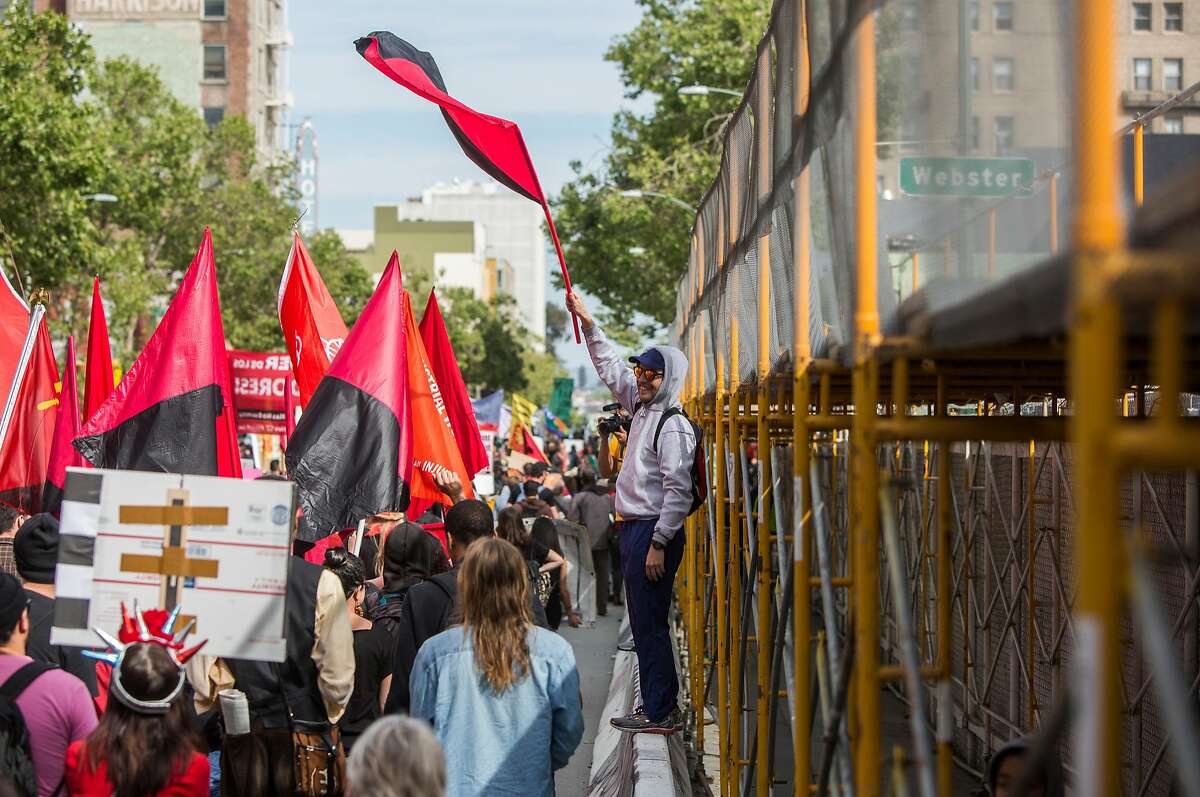 A man waves a flag while watching hundreds march down 14th Street during a May Day rally and march in Oakland, Calif. Tuesday, May 1, 2018