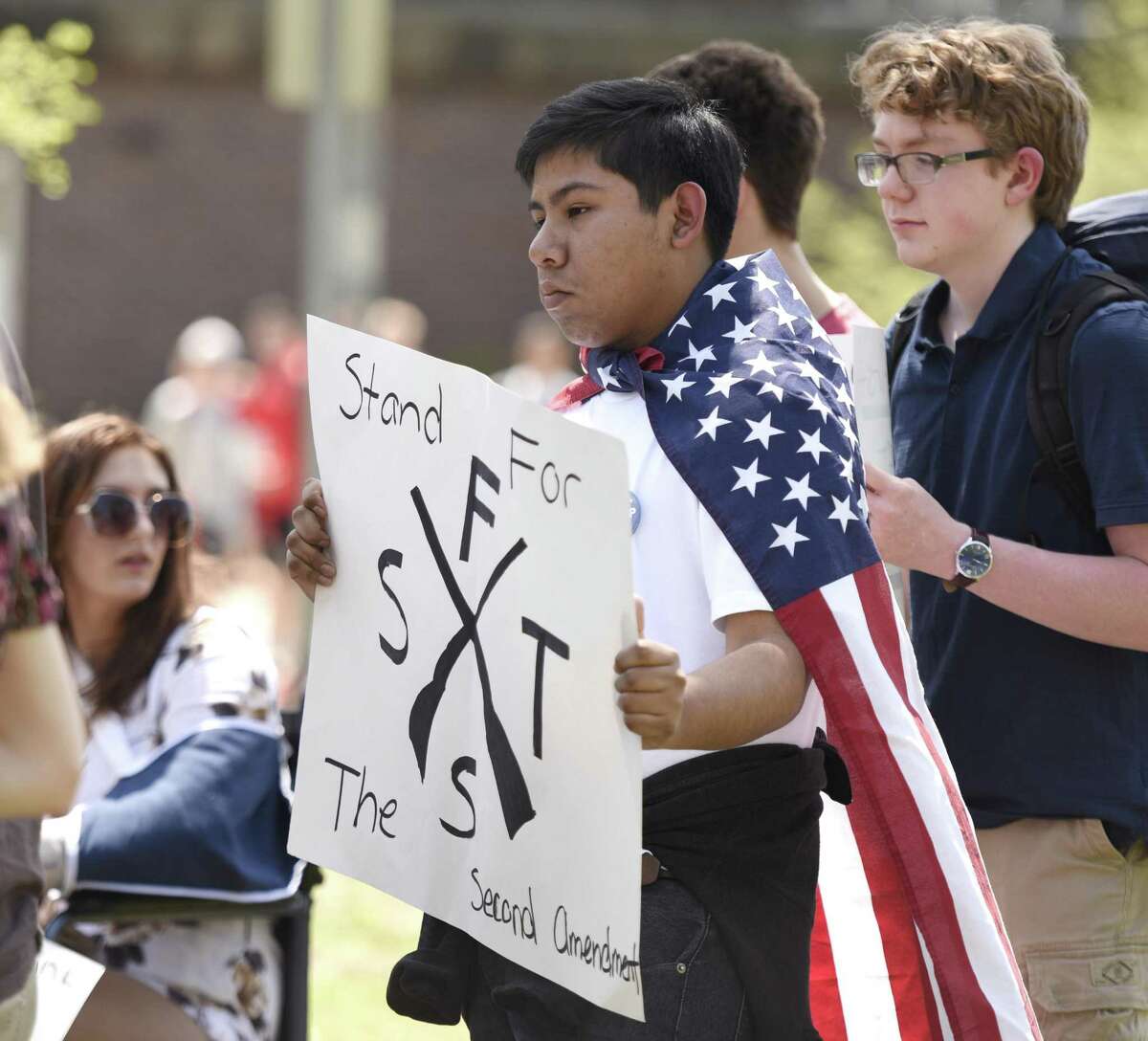 Sophomore Adrian Martinez dons an American flag and displays a sign during a pro-gun walkout at Greenwich High School in Greenwich, Conn. Wednesday, May 2, 2018. About a dozen students walked out of Greenwich High School armed with signs to make their voices heard and show support of the second amendment.