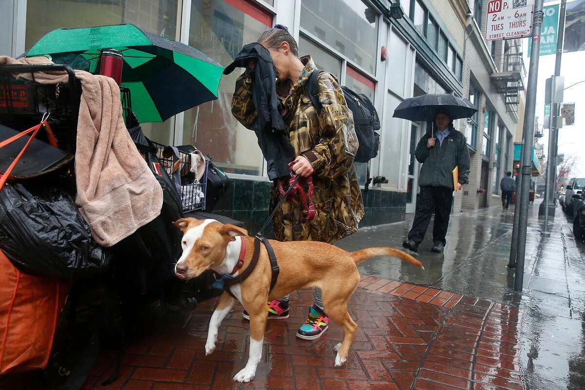 Amber Fina, who is homeless, wipes rain from her face as she stands with her dog, Ganja, on Grove Street before taking shelter from the rain in Burger King on Monday, January 8, 2018 in San Francisco, Calif.