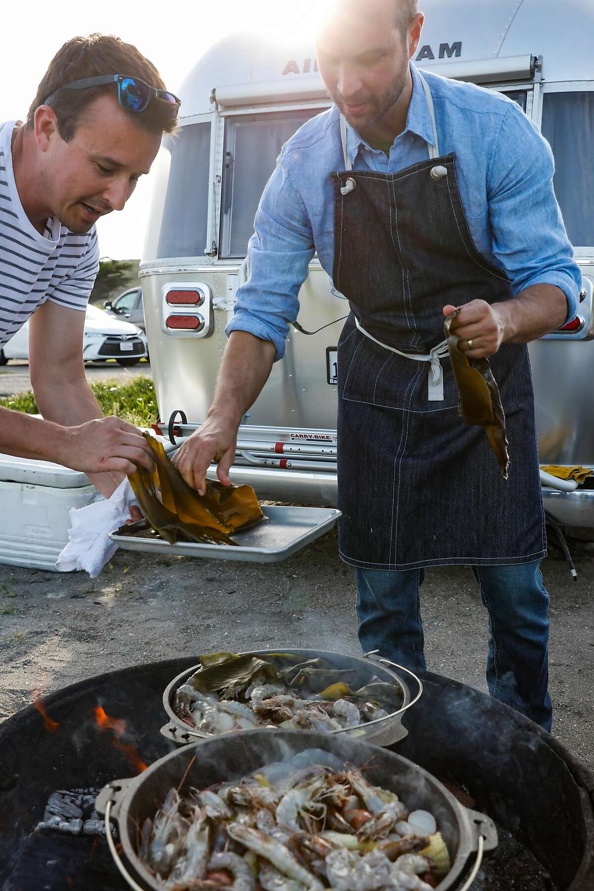 Chef de cuisine Robert Dort and Chef Ethan Mantle of Componere Catering lay seaweed on top of California Clambake with Monterey clams, head-on shrimp, sausage, corn potatoes on Monday, April 9, 2018 in Bodega Bay, Calif.