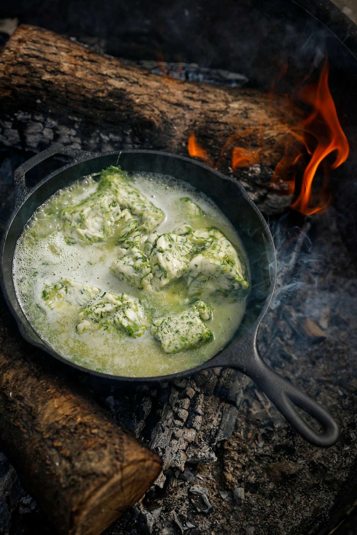 Green garlic butter melts in a cast iron pan over a fire on Monday, April 9, 2018 in Bodega Bay, Calif.