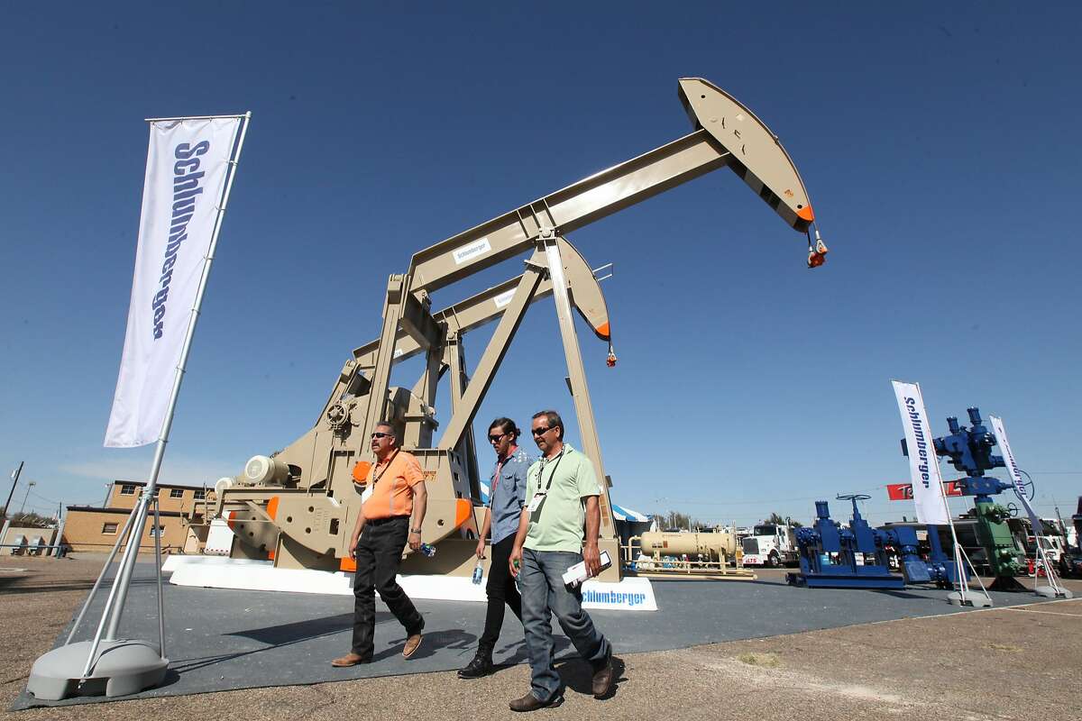 Oil show attendees walk past the Schlumberger booth at the Permian Basin International Oil Show at Ector County Coliseum on Tuesday, Oct. 18, in Odessa, Texas. NEXT: Scenes from a fracking and drilling operation.