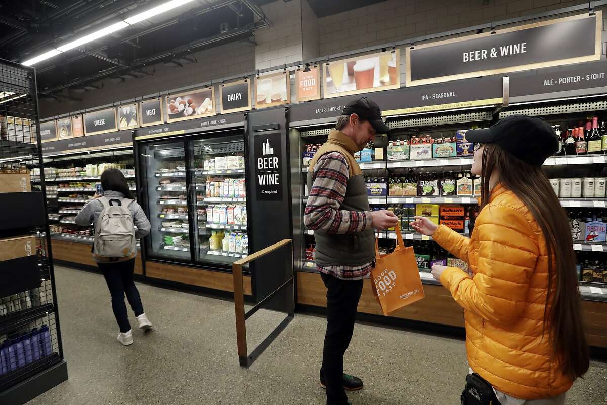 A worker, right, looks at the ID of a shopper at the wine and beer area inside an Amazon Go store Monday, Jan. 22, 2018, in Seattle. More than a year after it introduced the concept, Amazon opened its artificial intelligence-powered Amazon Go store in downtown Seattle on Monday. The store on the bottom floor of the company's Seattle headquarters allows shoppers to scan their smartphone with the Amazon Go app at a turnstile, pick out the items they want and leave. (AP Photo/Elaine Thompson)