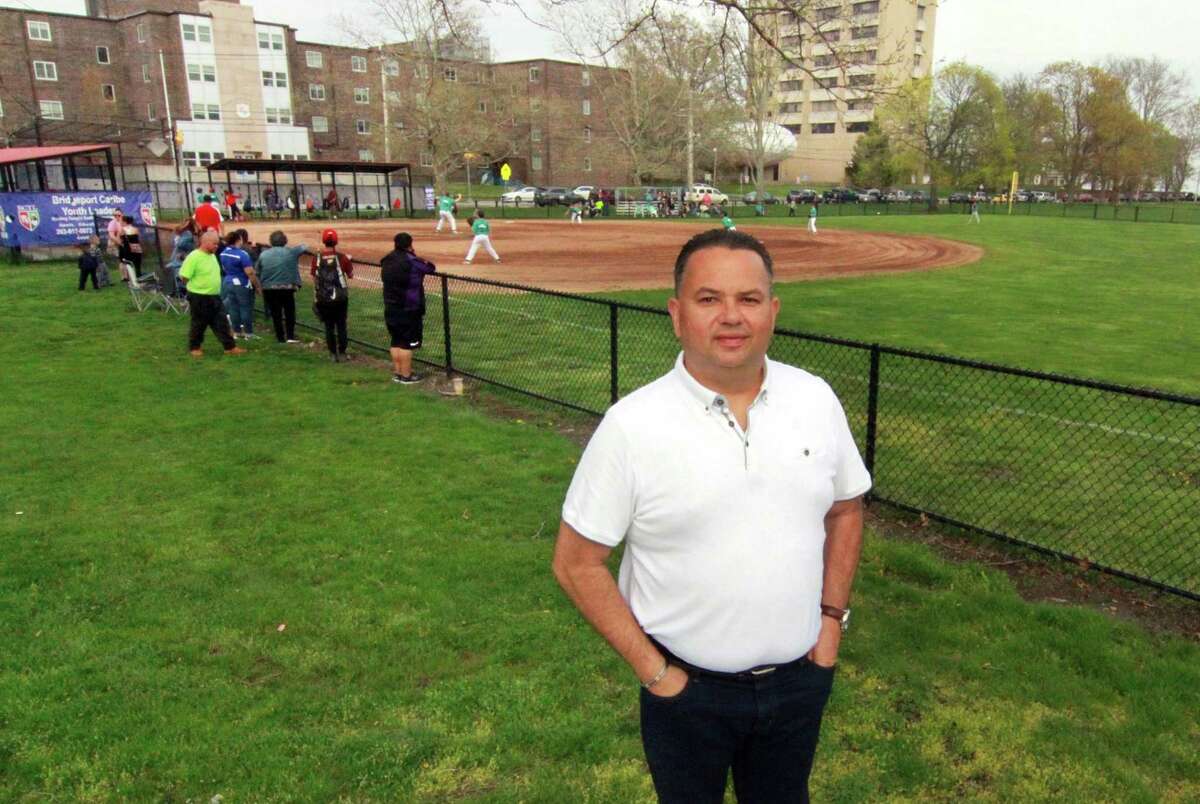 Bridgeport Caribe League Founder John Torres poses as a baseball game plays in the background at Seaside Park in Bridgeport, Conn., on Friday May 4, 2018. The organization is celebrating its 15th year. It has grown from strictly a baseball organization to where it now includes educational components.