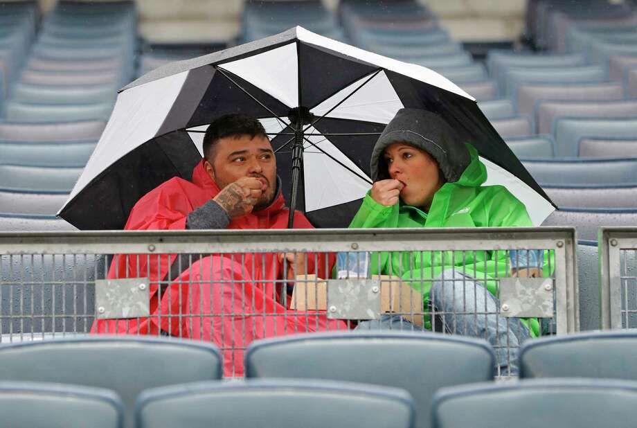 Two fans snack huddled under an umbrella during a rain-delayed baseball game between the New York Yankees and the Oakland Athletics in New York, Sunday, May 13, 2018. (AP Photo/Kathy Willens) Photo: Kathy Willens / Associated Press