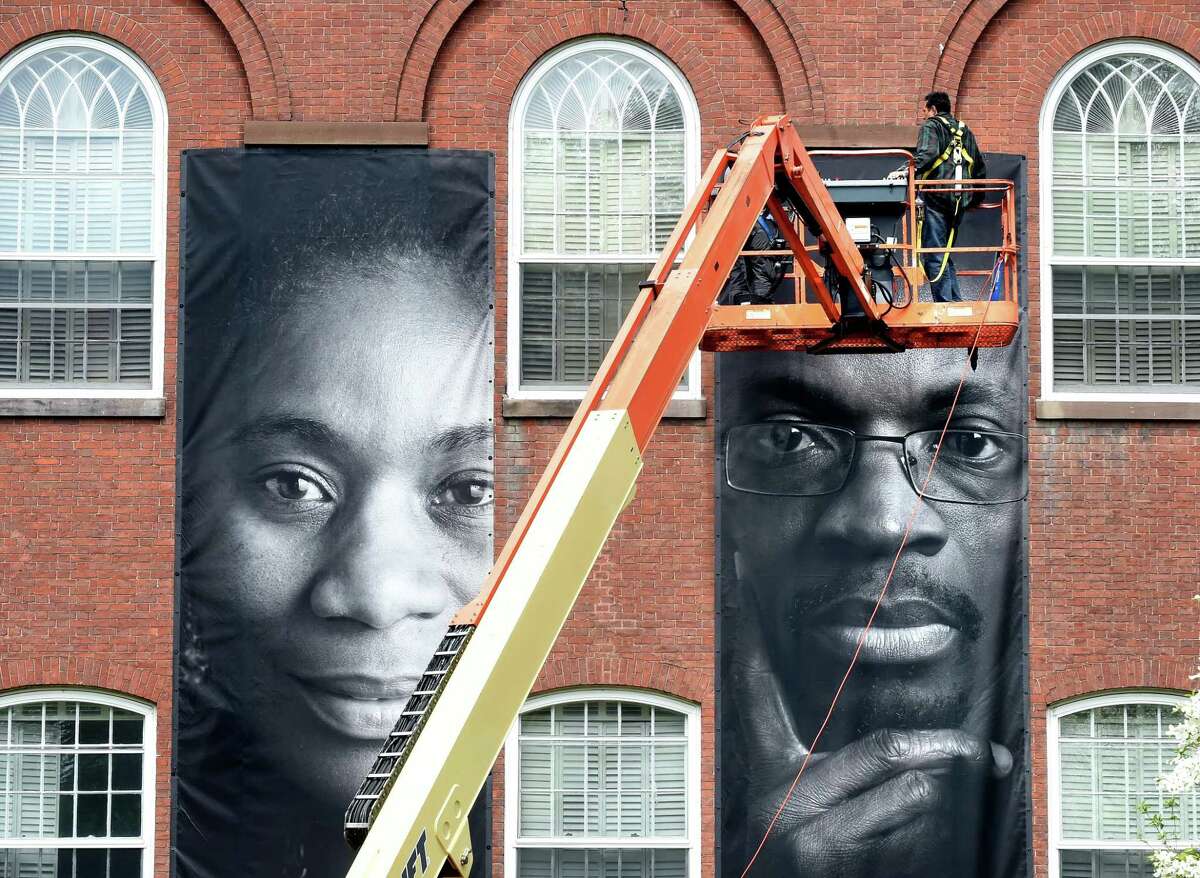 Workers install portraits of immigrants on United Church on the Green in New Haven Monday.