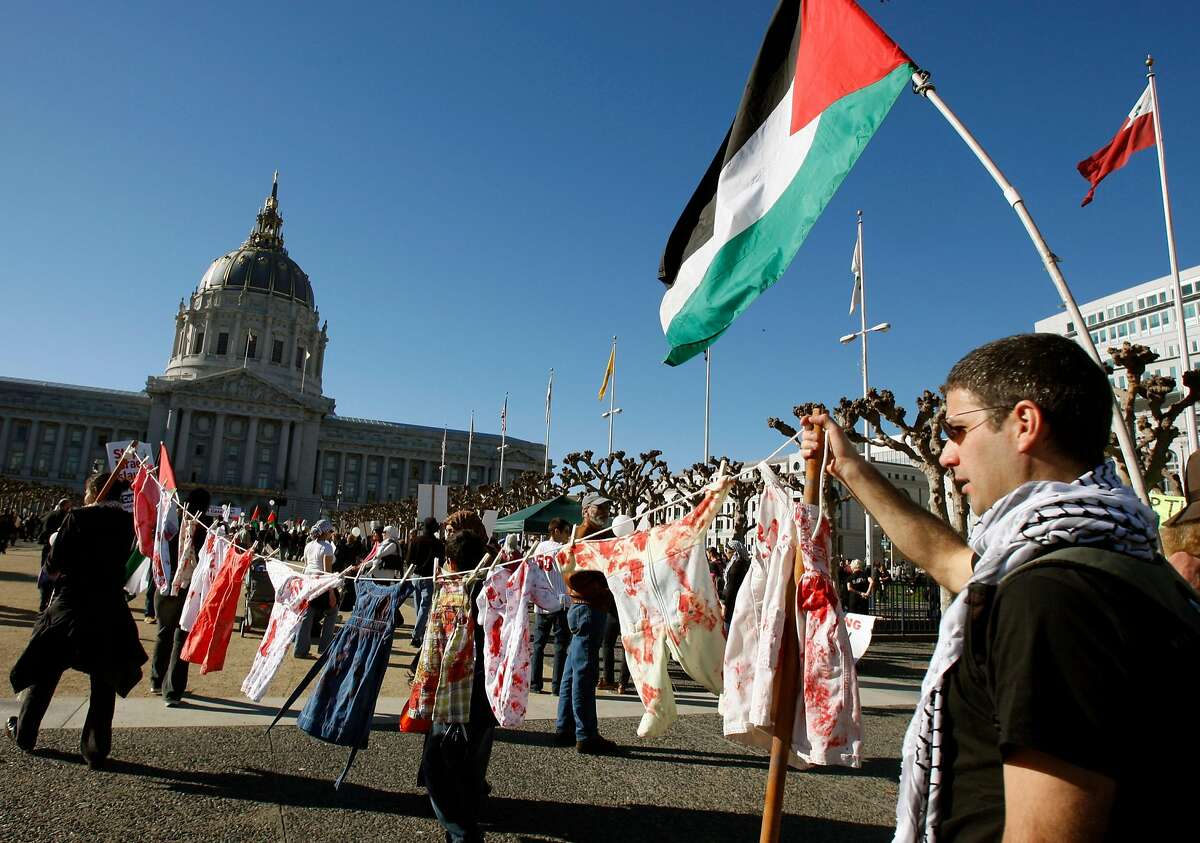 Amr Toppozada (right) carries a clothes line with children's clothing covered in mock blood with Sama Abuayyash (far left) at a pro-Palestinian rally at Civic Center Plaza in San Francisco, Calif., on Saturday, Jan. 10, 2009.