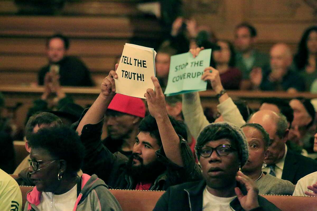 People hold up signs as they react during the Board of Supervisors' Land Use and Transportation Committee meeting during a hearing on the Hunters Point Shipyard clean-up on Monday, May 14, 2018 in San Francisco, Calif.