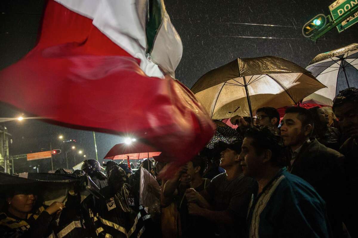 Supporters of Andres Manuel Lopez Obrador, presidential candidate of the National Regeneration Movement Party (MORENA), wave the Mexican flag during the first presidential debate outside the Palace of Mining in Mexico City, Mexico, on Sunday, April 22, 2018. Mexico's peso, the world's best-performing currency this year, could depreciate as attention turns from NAFTA optimism to changes associated with presidential front-runner Lopez Obrador.