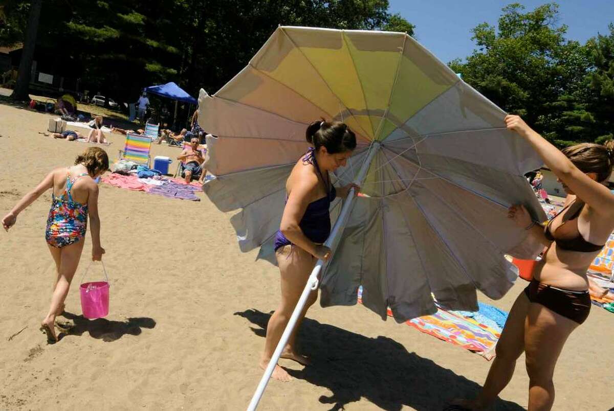 Jen McDade, center, of Clifton Park, and her sister-in-law Catherine McDade set up an umbrella at the beach on the lake at Moreau State Park.( Michael P. Farrell / Times Union )