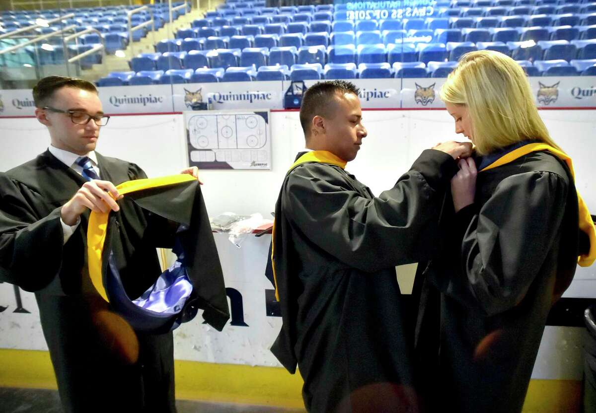 Hamden, Connecticut - Saturday, May 19, 2018: Classmates Shane Sullivan of Milford, left, Pavel Aragon of Wallingford, center, and Nora Winkler of Madison, right, put on their graduation attire before the start of the 87th Quinnipiac University undergraduate commencement exercises for the School of Business Saturday afternoon at Quinnipiac's TD Bank Sports Center in Hamden.