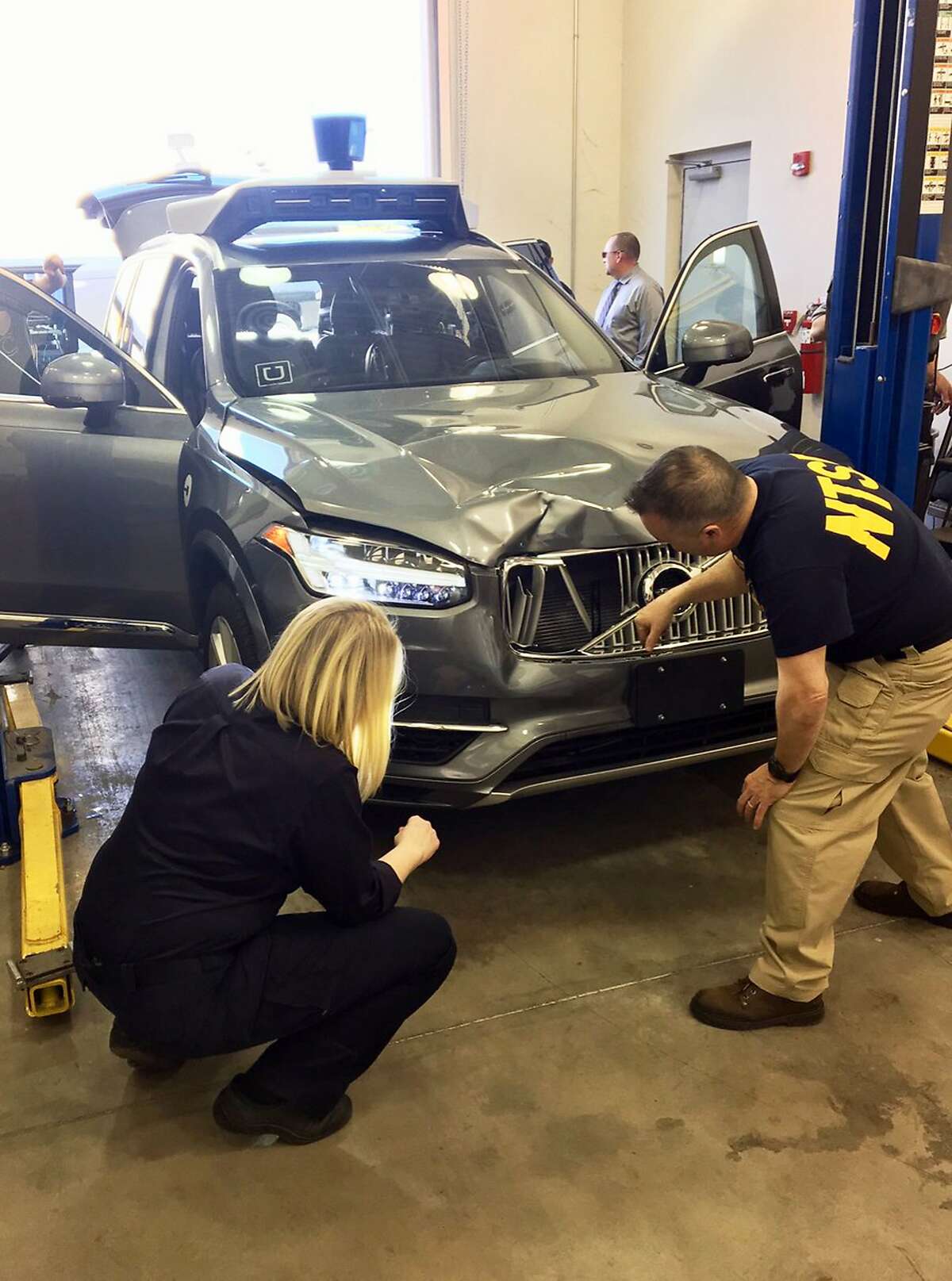 FILE- In this March 20, 2018, file photo provided by the National Transportation Safety Board, investigators examine a driverless Uber SUV that fatally struck a woman in Tempe, Ariz. Uber announced Wednesday, May 23, that it is pulling its self-driving cars out of Arizona, a reversal triggered by the recent death of woman who was run over by one of the ride-hailing service's robotic vehicles while crossing a darkened street in a Phoenix suburb. (National Transportation Safety Board via AP, File)