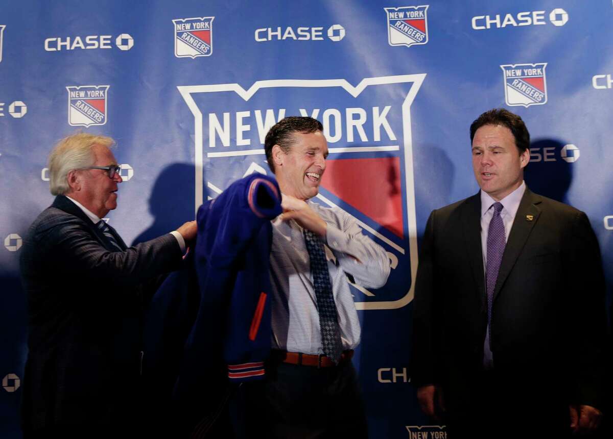 The New York Rangers new head coach David Quinn, center, puts on a team jacket while team president Glen Sather, left, and general manager Jeff Gorton look on during an NHL hockey news conference in New York, Thursday, May 24, 2018. (AP Photo/Seth Wenig)