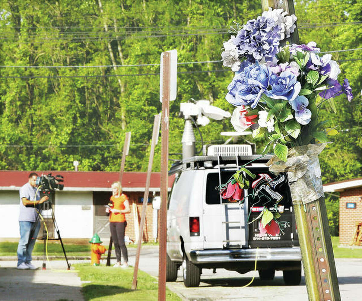 A television news reporter does a live broadcast Tuesday near the scene of a double homicide late Monday in Alton Acres, in the shadow of memorial flowers left up for 11-year-old Romell Jones who was killed in January 2016 in a drive-by shooting less than 100 yards away from Tuesday’s scene.