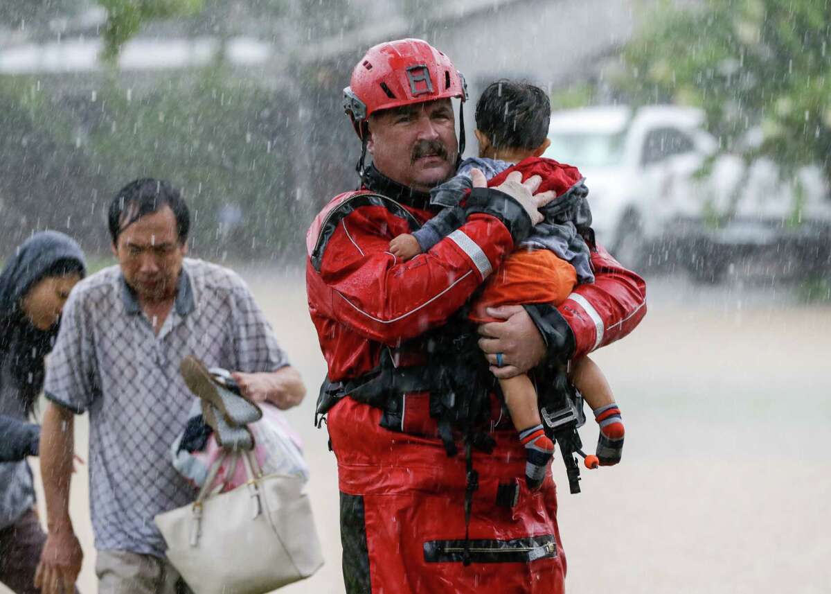 Chad Smith, a Task Force One member from the Dallas Fire Department, carries 1-year-old Christian Rodriguez from a rescue boat as people are transferred to a pickup point along Edgebrook in Houston on Sunday, August 27, 2017, after Hurricane Harvey inundated the area.