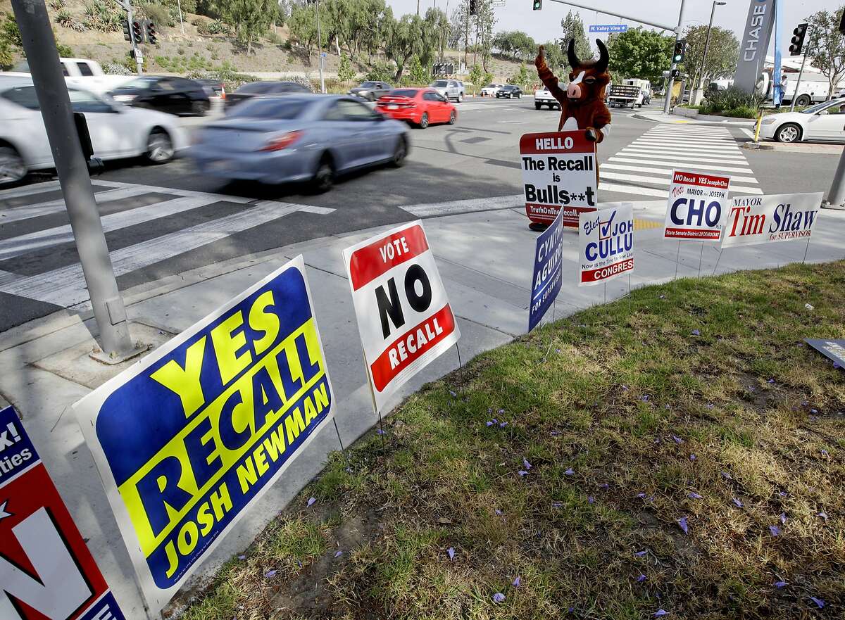 In this May 30, 2018 photo, a person in a bull suit, standing amid campaign signs, urges voters to reject the recall campaign launched against Democratic California state Senator Josh Newman, on a street in Fullerton, Calif. Newman in fight for his political life as Republicans seek to oust him over his vote, along with 80 other legislators, to raise California's gas tax. (AP Photo/Chris Carlson)