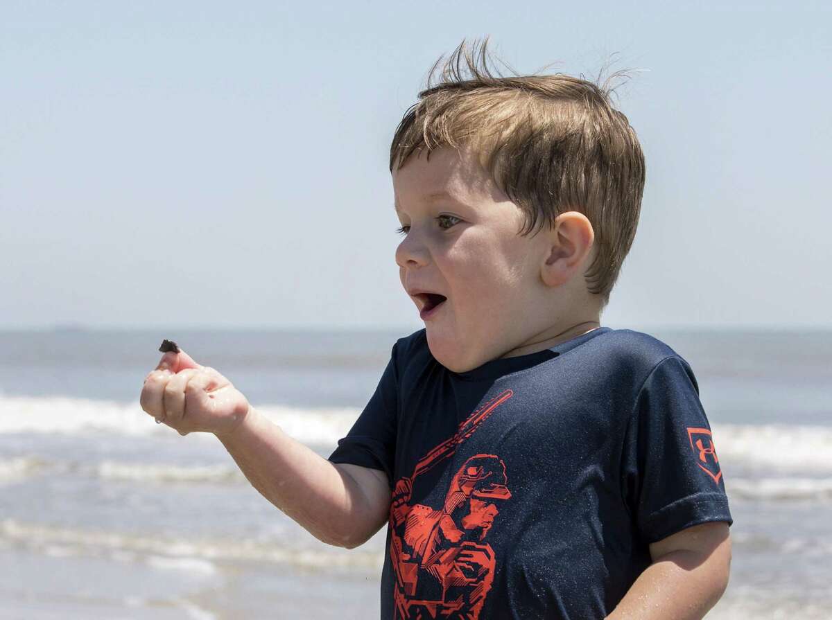 Collin Doggett, 4, who traveled from Decatur, Texas with his family to spend time at the beach, finds a seashell he likes as he plays in the surf for the first time.