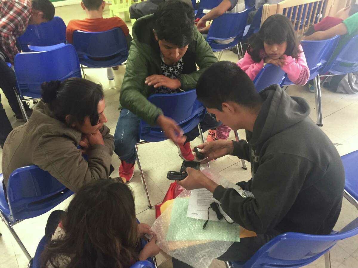 Migrants show Santiago Choc Chomo, a Guatemalan father who was briefly separated from his 10-year-old daughter, how to charge his electronic ankle monitoring bracelet. He was released and rejoined with the girl because immigration officials had no more space to hold him.