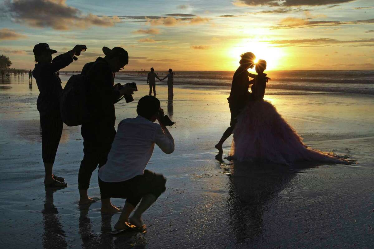  In this Jan. 18, 2017, file photo, photographers take photos of a tourist couple's wedding at the famous Kuta beach during sunset in Bali, Indonesia. According to a 2016 survey from wedding site The Knot, the average cost of an international destination wedding is $25,800. That figure may be within your event budget, but for guests, international airfare and multinight lodging could be out of reach. (AP Photo/Firdia Lisnawati, File)