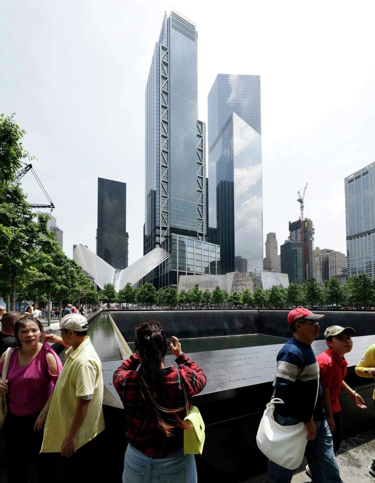 In this June 8, 2018 photo, 3 World Trade Center towers above visitors at the September 11 Memorial in New York. The center's latest skyscraper opens Monday. (AP Photo/Mark Lennihan)