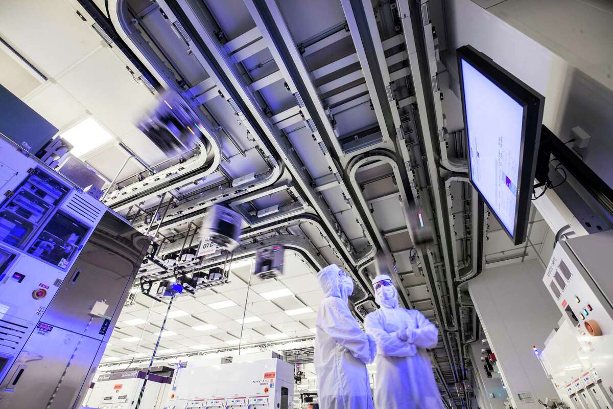 Workers at GlobalFoundries' computer chip factory in Malta. Above them are the motorized tracts that carry the containers known as "foups" in which silicon wafers are transported.